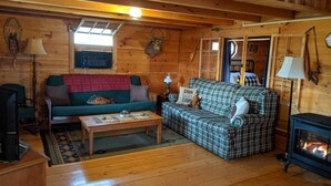 A cozy cabin interior with a wooden floor, two plaid sofas, a coffee table, a fireplace, and a mounted deer head. - Amish-Built Cabin in the Driftless Area (Boscobel)