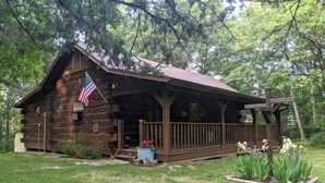 A rustic log cabin with an American flag, a porch, and a small garden with flowers. - Amish-Built Cabin in the Driftless Area (Boscobel)
