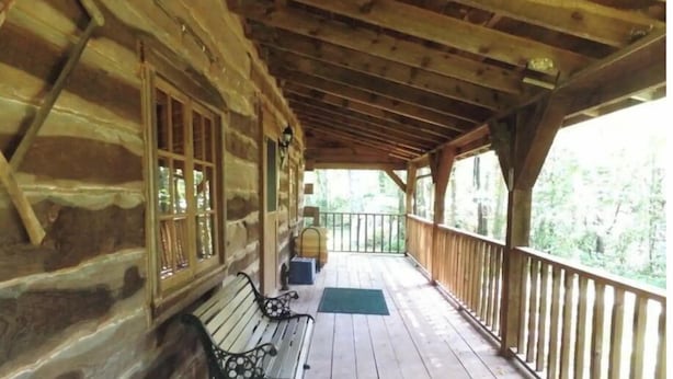 A wooden cabin with a covered porch, two benches, and a view of the forest. - Amish-Built Cabin in the Driftless Area (Boscobel)