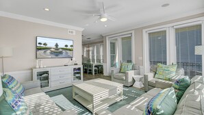 A spacious living room with a flat-screen TV, a ceiling fan, and a dining area with a table and chairs.