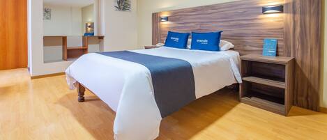 A neatly arranged hotel room with a large bed, wooden headboard, bedside tables, and a mirror.