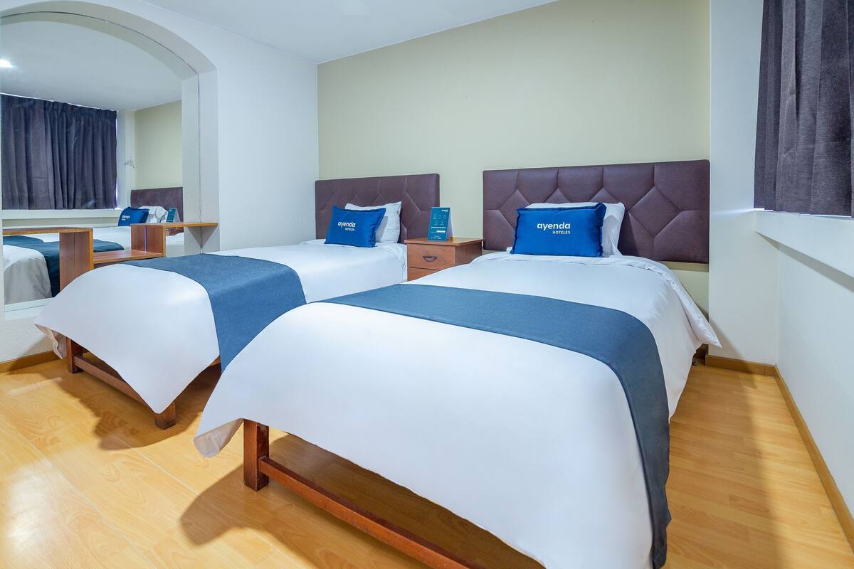 A hotel room with two beds, a wooden floor, a mirror, and a nightstand with a phone.