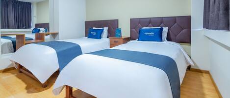 A hotel room with two beds, each with a blue pillow and a wooden nightstand.