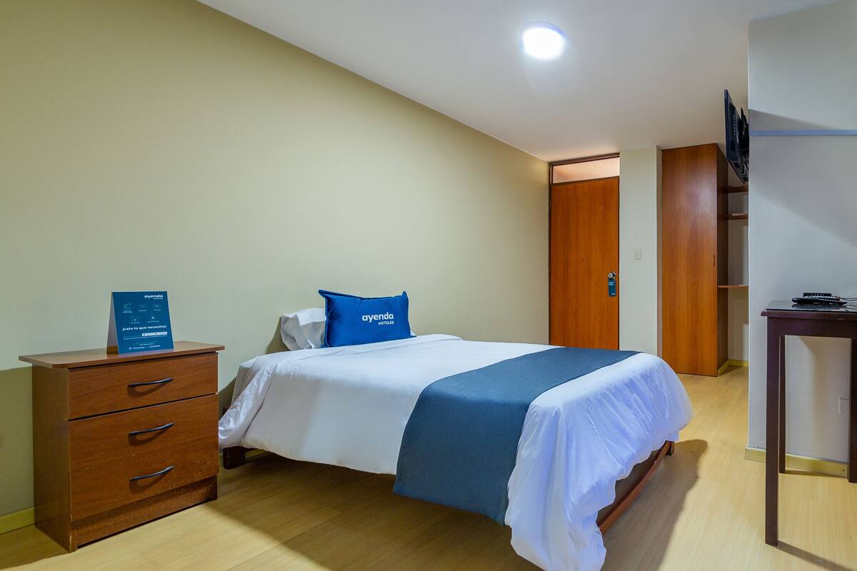A hotel room with a bed, a wooden dresser, a desk, and a television on a stand.