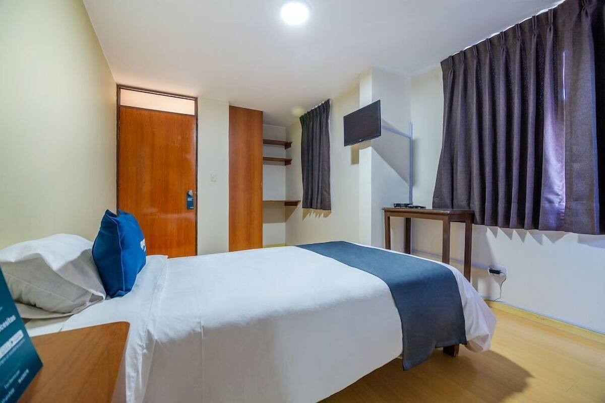 A hotel room with a bed, a desk, a TV, and a window with curtains.