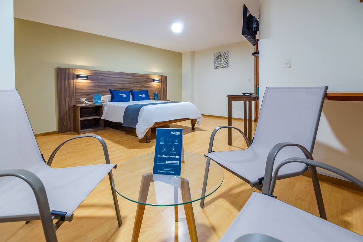 A hotel room with a bed, two chairs, a small table, and a TV.