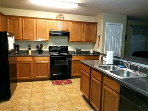 Una cocina con armarios de madera, una estufa negra, un lavamanos y un refrigerador.