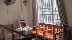 A room with a wooden bench, a table with teapots and cups, a water dispenser, and a window with curtains. - A25 Hotel New Asean (Hanoi)