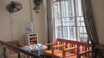 Una habitación con un banco de madera, una mesa con teteras y tazas, un dispensador de agua y una ventana con cortinas.