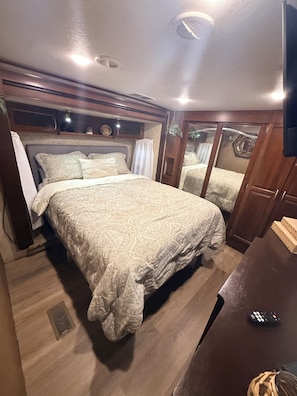 A bedroom with a large bed, a wooden headboard, a small table, and a television.