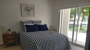 Un dormitorio con cama, mesita de noche, cómoda, un cuadro en la pared y una puerta corrediza de vidrio que da a un balcón.