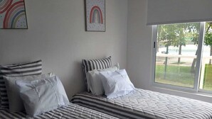 Habitación con dos camas, ropa de cama a rayas, ventana con vistas y aire acondicionado instalado en la pared.