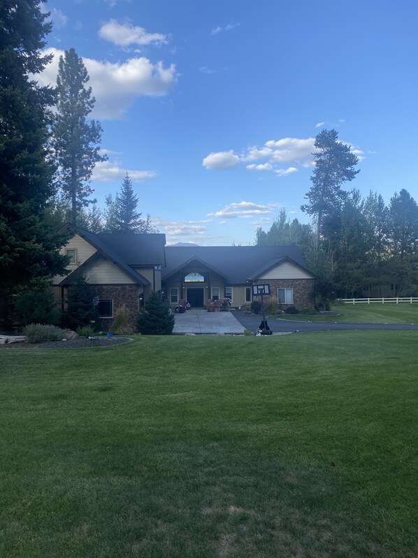 A two-story house with a central archway entrance, surrounded by a well-maintained lawn and tall trees.