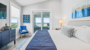 A bedroom with a large bed, a blue chair, a dresser, and a view of the ocean through a glass door. - Luxury Gulf-Front Retreat. Heated Pool, Pet-Friendly.  (Cape San Blas)