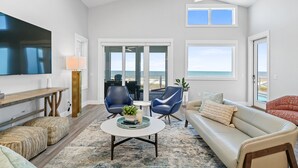 A spacious living room with a large flat-screen TV, comfortable seating, and a view of the beach. - Luxury Gulf-Front Retreat. Heated Pool, Pet-Friendly.  (Cape San Blas)