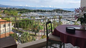 Ein Balkon mit Tisch und Stuhl mit Blick auf einen Yachthafen, Boote und eine ferne Skyline.
