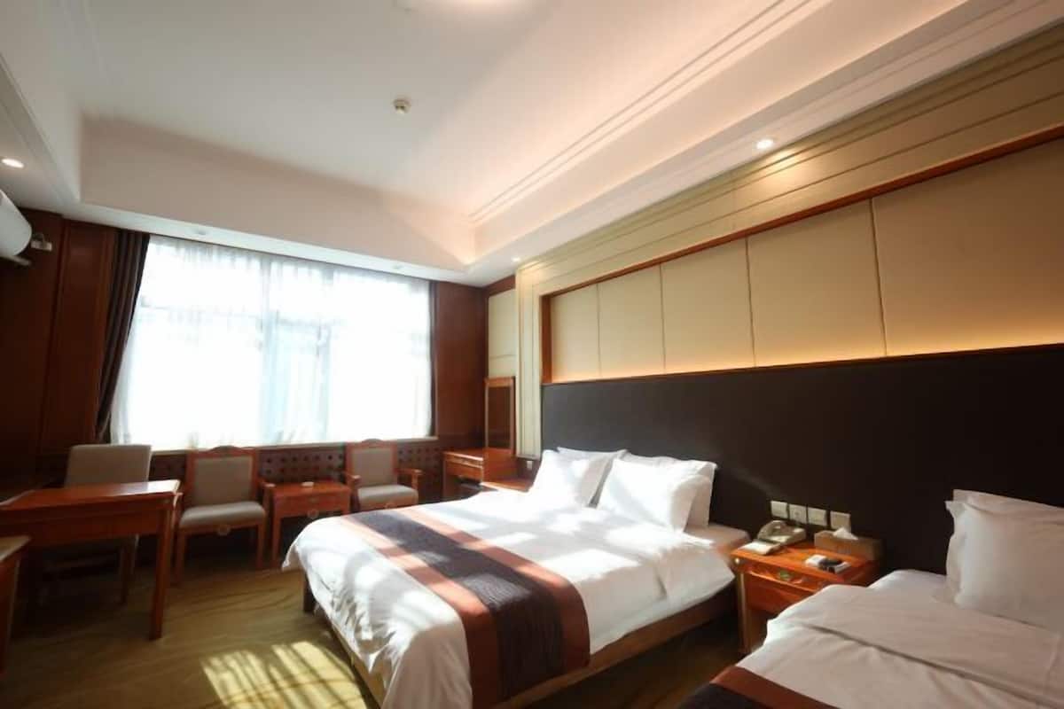 A hotel room with a large bed, a desk, a chair, a nightstand, and a window with curtains.