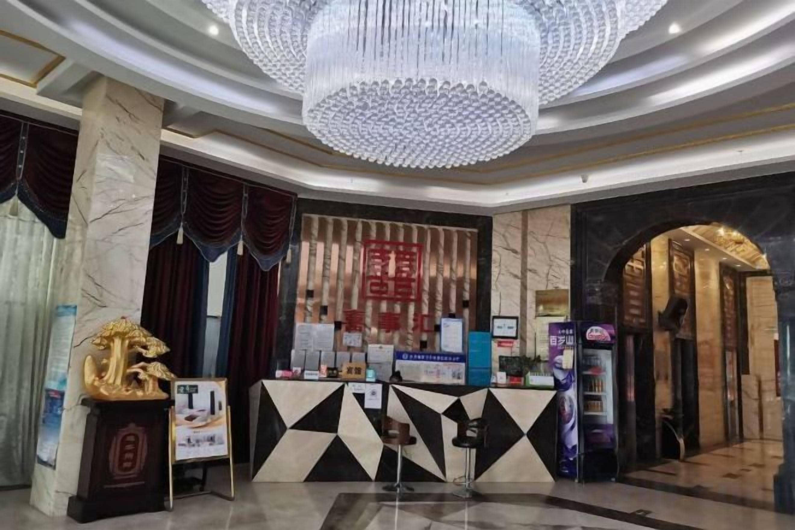 A hotel lobby with a reception desk, a chandelier, and a traditional Chinese wall.