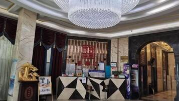 A hotel lobby with a reception desk, a chandelier, and a traditional Chinese wall.