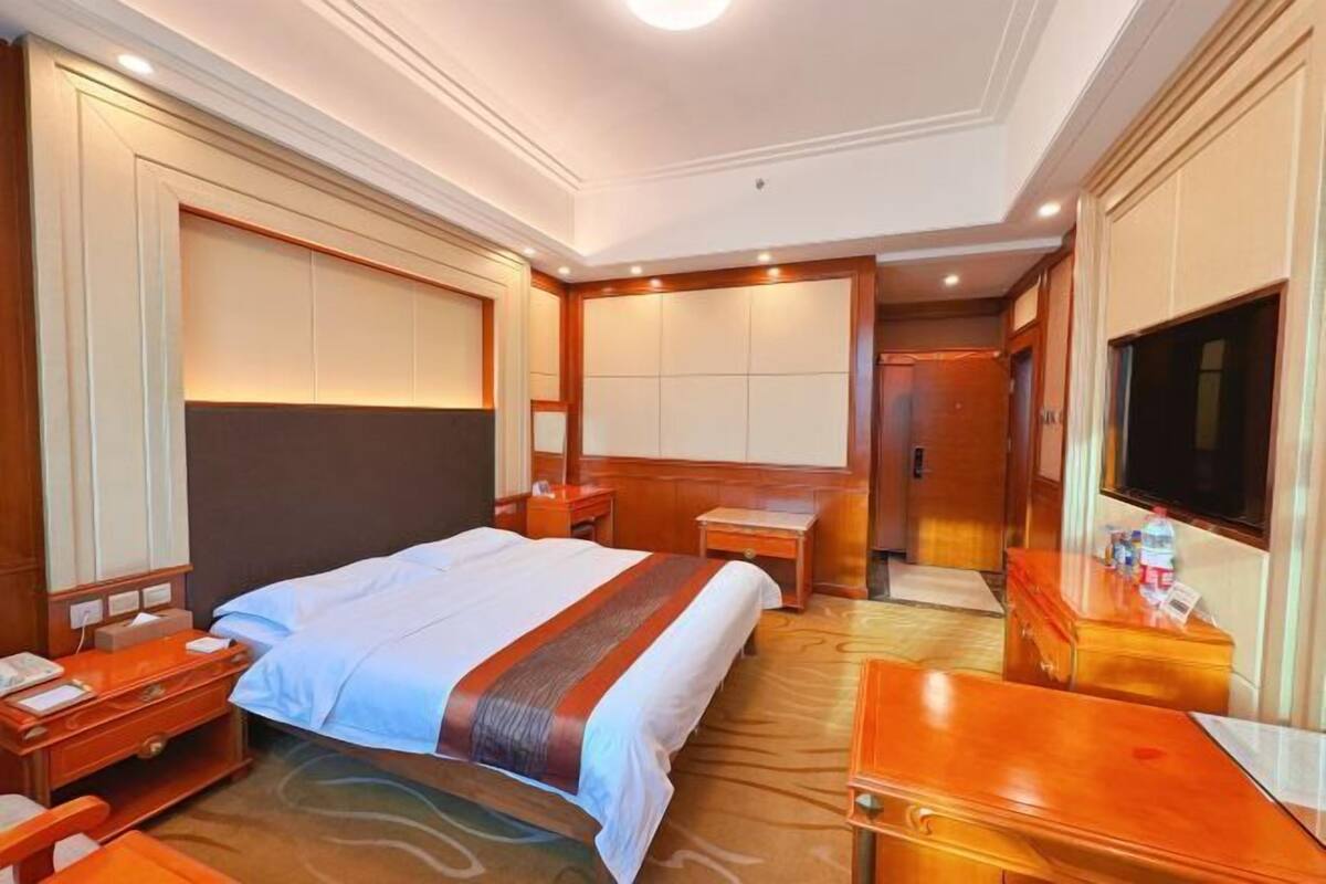 A hotel room with a large bed, a desk, a TV, and a wardrobe.