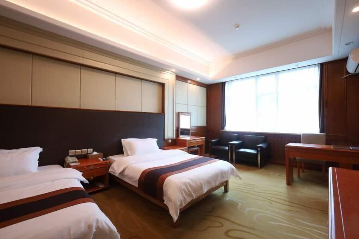 A hotel room with two beds, a desk, a chair, and a large window.