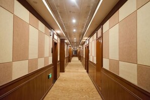 Un pasillo de hotel con paneles de madera, pisos alfombrados y puertas que dan a las habitaciones.