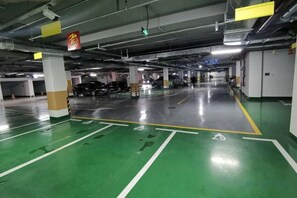 A multi-level parking garage with green and white parking spaces, concrete pillars, and overhead lighting. - Xishihui Hotel (Mishan)