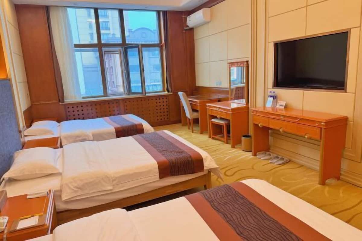 A hotel room with two beds, a desk, a chair, a television, and a window with a view of buildings.