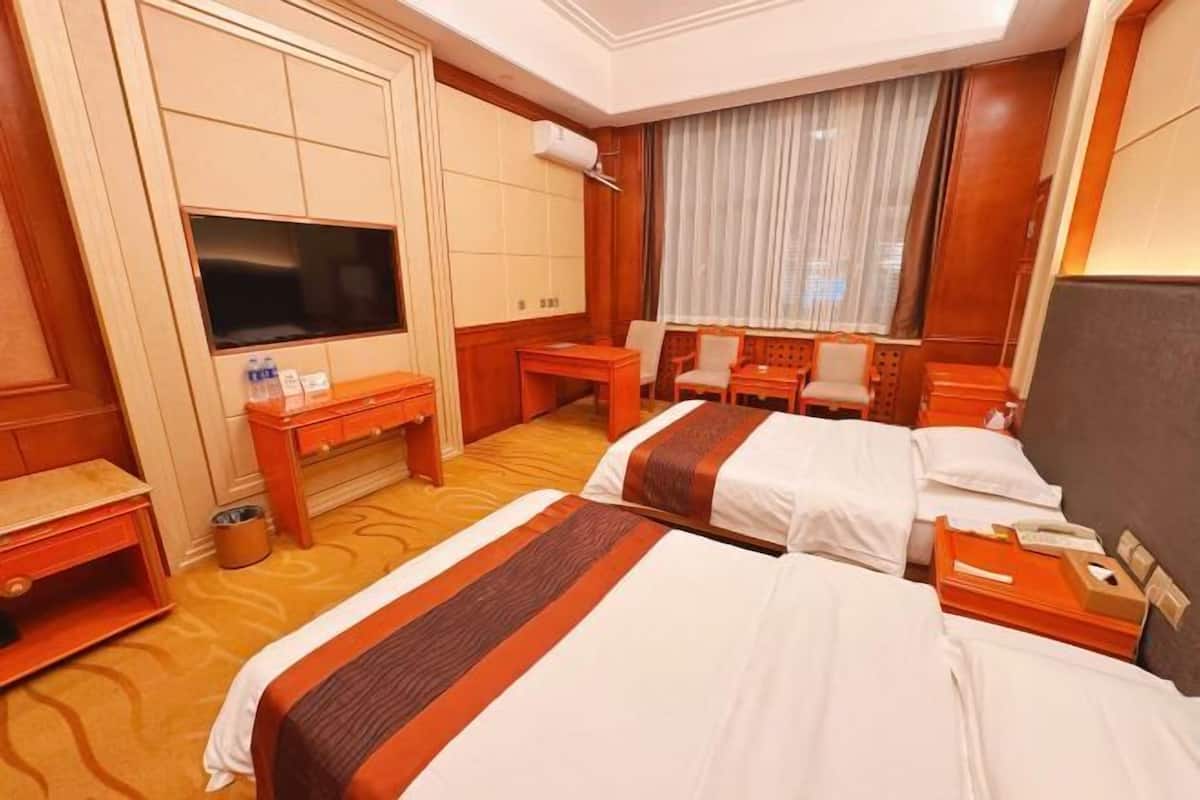 A hotel room with two beds, a TV, a desk, and a window with curtains.
