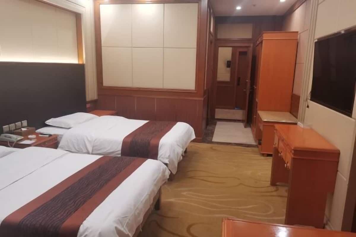 A hotel room with two beds, a wardrobe, a desk, and a television.