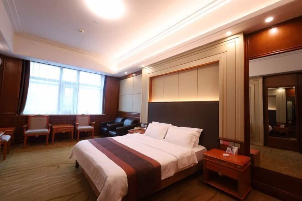 A hotel room with a large bed, a desk, a chair, and a window.