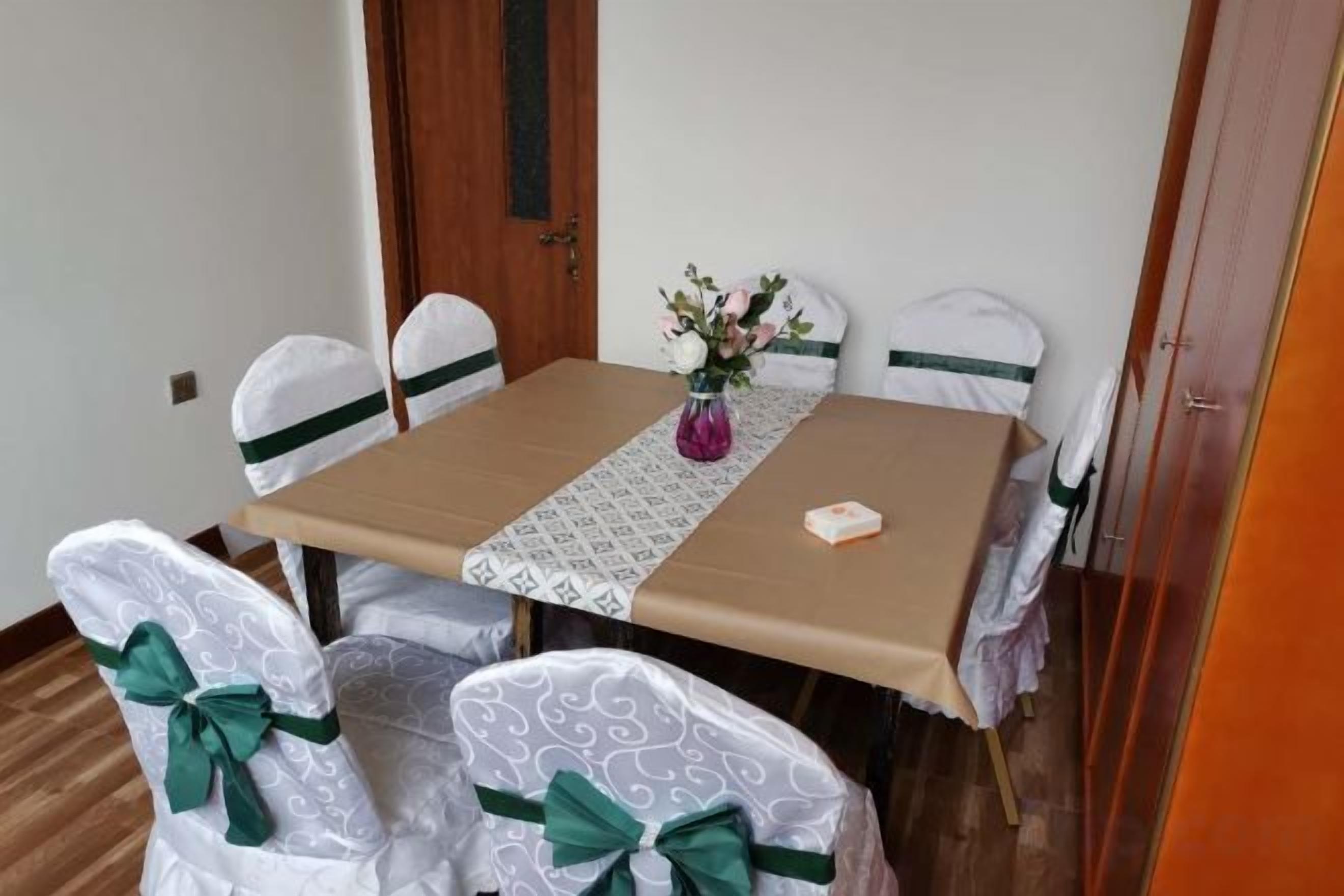 Une table à manger agrémentée d’un chemin de table à motifs, des chaises décorées de nœuds et un vase rempli de fleurs.