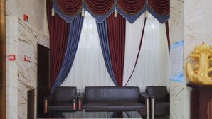 A lobby with marble walls, two black leather sofas, red and blue drapes, and a golden statue. - Xishihui Hotel (Mishan)