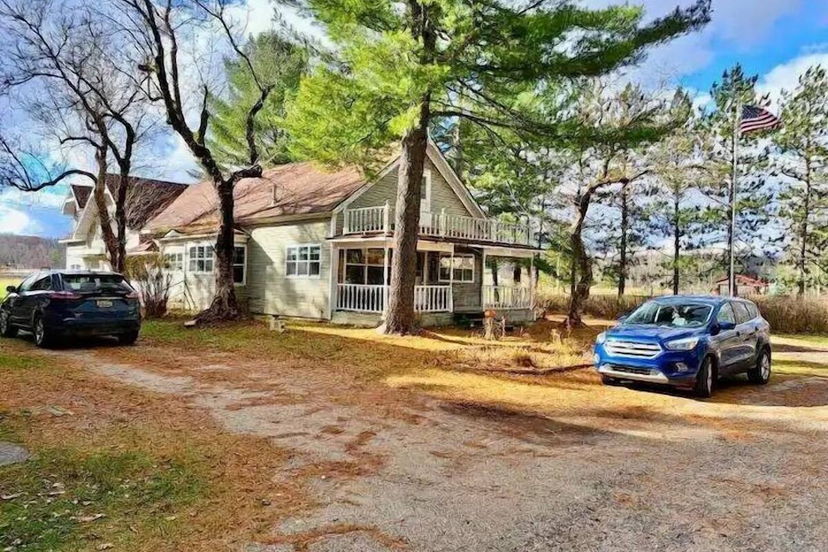 A two-story house with a porch, a driveway, and two parked cars.