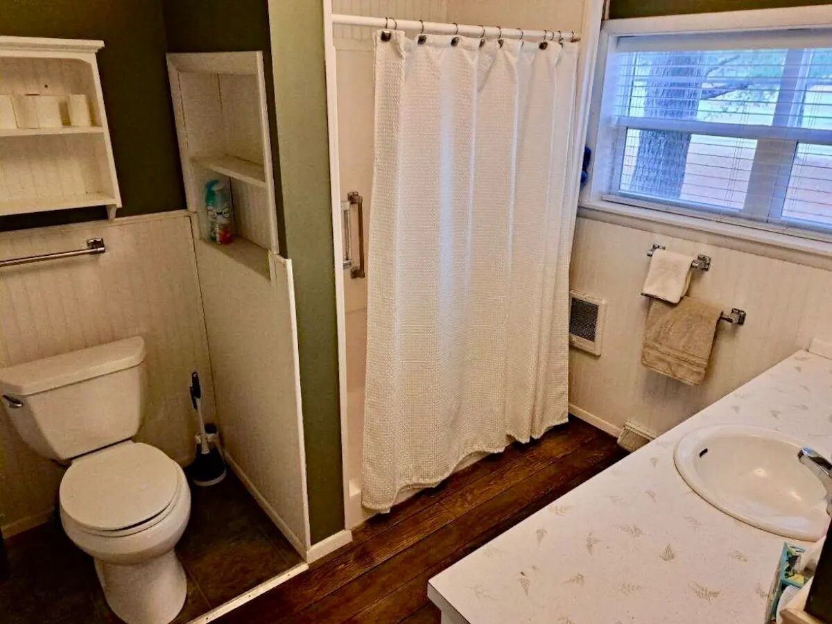 Un baño con inodoro, cortina de ducha, lavamanos y ventana.