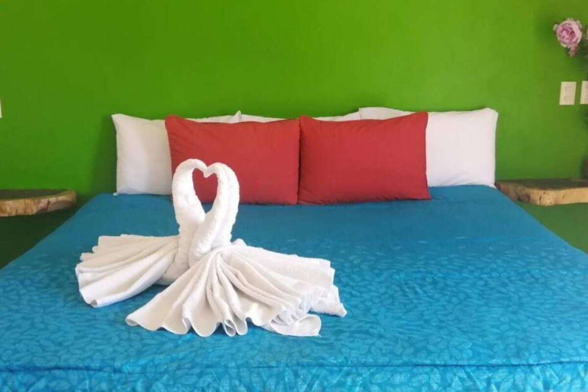 A bed with a blue bedspread, white pillows, and a heart-shaped towel arrangement.