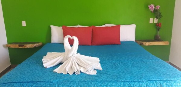 Una cama con una colcha azul, almohadas blancas y un arreglo de toallas con forma de corazón.