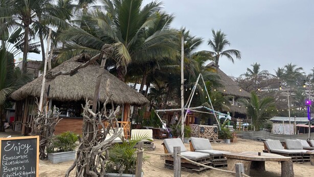 Un restaurant situé en bord de mer, avec des huttes à toit de chaume, des chaises longues et un panneau affichant le menu.