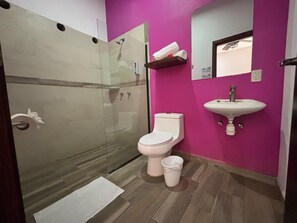 Un baño con cabina de ducha de vidrio, inodoro, lavamanos y pared rosa.