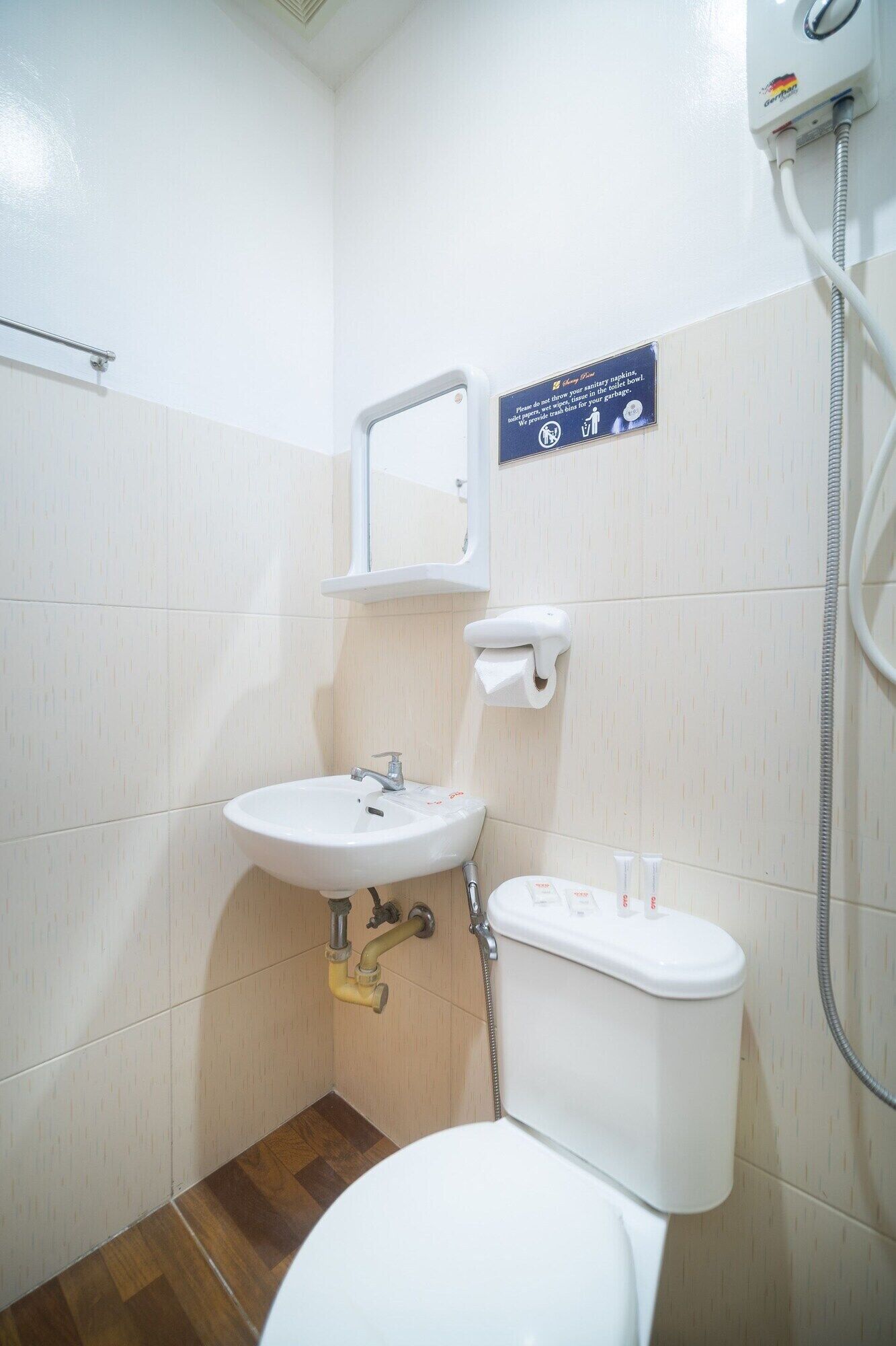 Un baño pequeño y limpio con un lavabo blanco, espejo y váter. Hay un cartel que indica no tirar tampones ni compresas en la taza del inodoro.