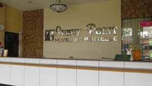 Mostrador de recepción en Sunny Point Hotel & Apartment con un fondo de pared de piedra y un reloj a la izquierda.