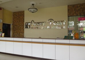 A reception desk at Sunny Point Hotel & Apartment with a stone wall backdrop and a clock on the left. - Sunny Point Hotel & Apartelle (Davao)