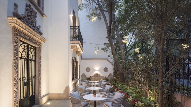 An outdoor patio with round tables and chairs, surrounded by plants and decorative lighting. - Casa Cleo Boutique Stays by Viadora (Mexico City)