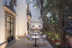 An outdoor patio with round tables and chairs, surrounded by plants and decorative lighting. - Casa Cleo Boutique Stays by Viadora (Mexico City)