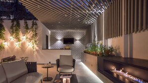 A modern outdoor seating area with a sofa, a chair, a small round table, and a built-in fire feature. - Casa Cleo Boutique Stays by Viadora (Mexico City)