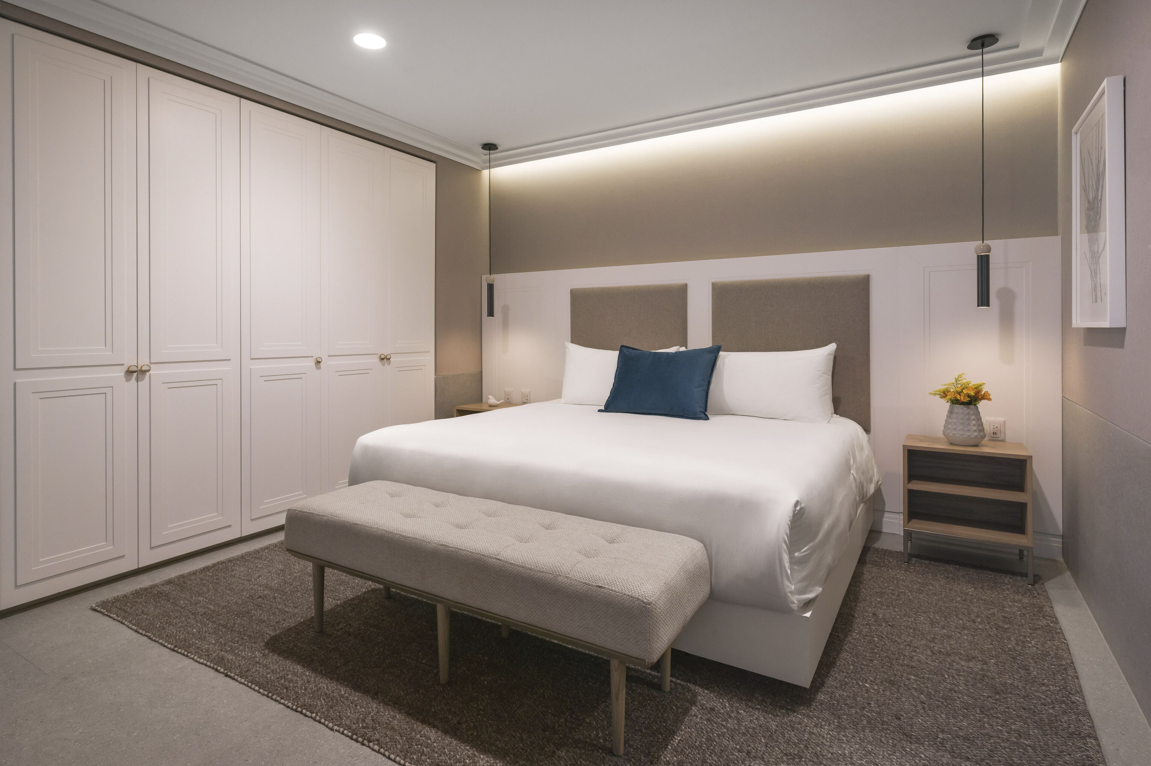A modern bedroom with a large bed, a bench, a nightstand, and a wardrobe.