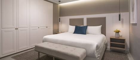 A modern bedroom with a large bed, a bench, a nightstand, and a wardrobe.
