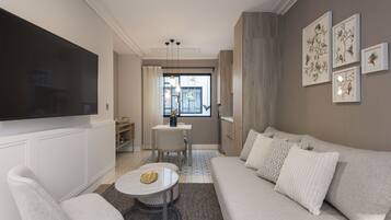 A modern living room with a sofa, armchair, and coffee table, a flat-screen TV, and artwork on the wall.