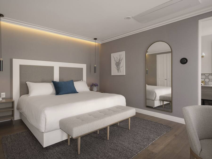 Um quarto moderno com uma cama grande, um banco, uma mesa de cabeceira, um espelho e um criado-mudo.