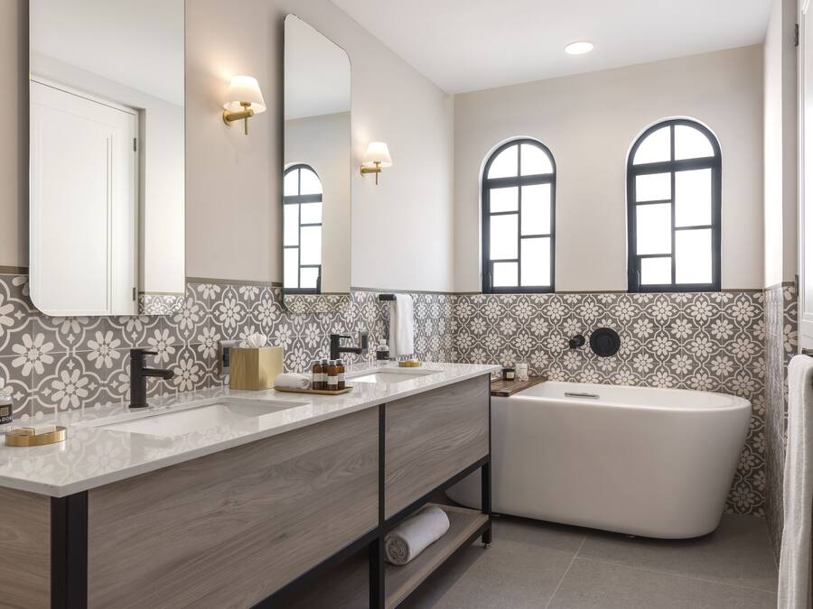 Un baño moderno con un espejo grande, dos lavamanos, una bañera y paredes con azulejos estampados.
